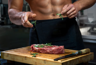 Perfectly Naked, Sexy chef with naked body cooking or decorating raw meat with rosemary in the restaurant kitchen