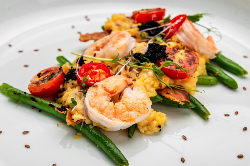 Omelet with shrimp, caviar and grilled tomatoes on a bed of asparagus beans and bacon. Serving food in a restaurant. Healthy food concept