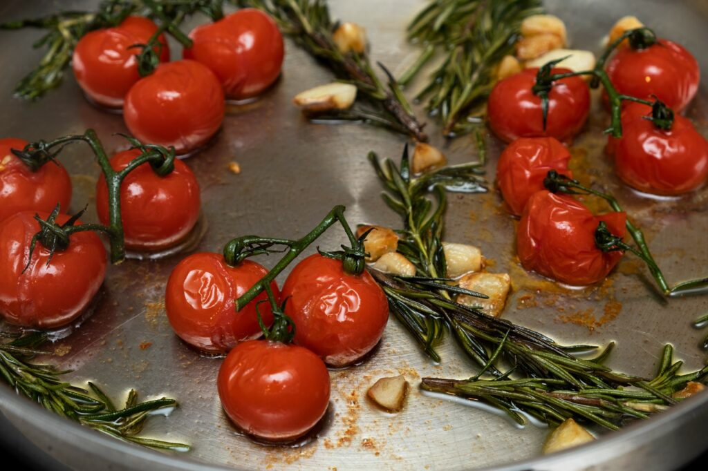 Cherry tomatoes fried in a frying pan with rosemary and garlic, close-up, selective focus